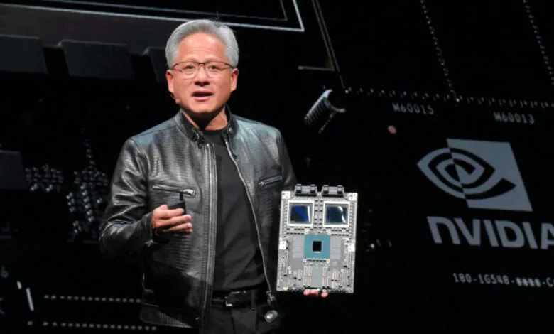 Jensen Huang holds a circuit board in front of an Nvidia backdrop.