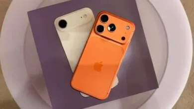 Orange and white iPhones with unique camera designs on purple and white surface.