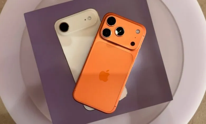Orange and white iPhones with unique camera designs on purple and white surface.