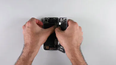 Hands carefully open a smartphone, revealing its internal components.