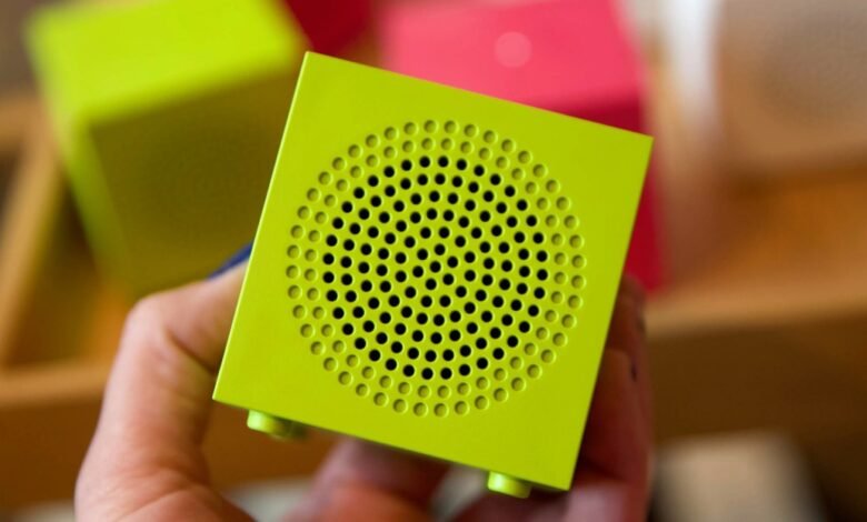 Hand holds a small, bright green cube speaker with circular grill.