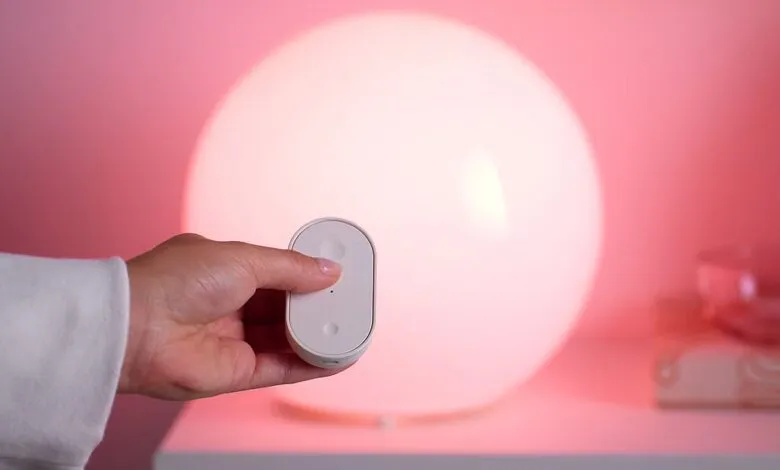 Hand holding remote controlling a round, glowing lamp.