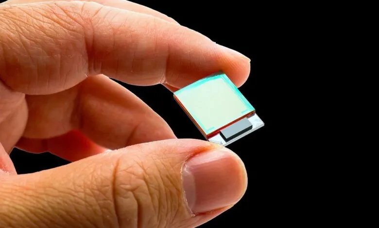 Hand holding a small, square microchip against a black background.