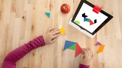 Child playing tangram puzzle game on tablet with wooden pieces.
