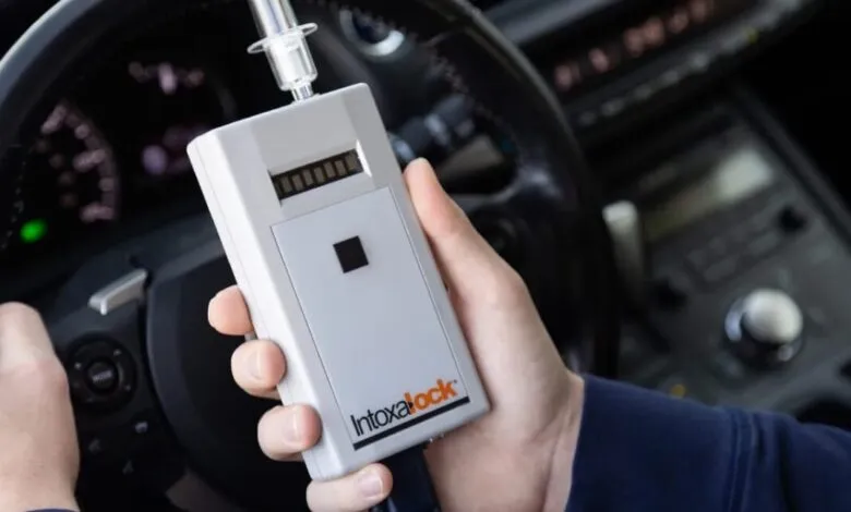 Hand holding Intoxalock device inside car, testing alcohol level.