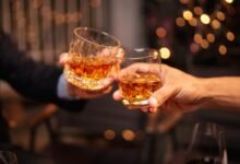 Two people toasting with glasses of amber liquor.