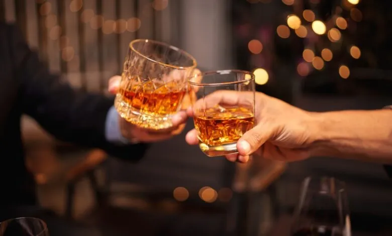 Two people toasting with glasses of amber liquor.