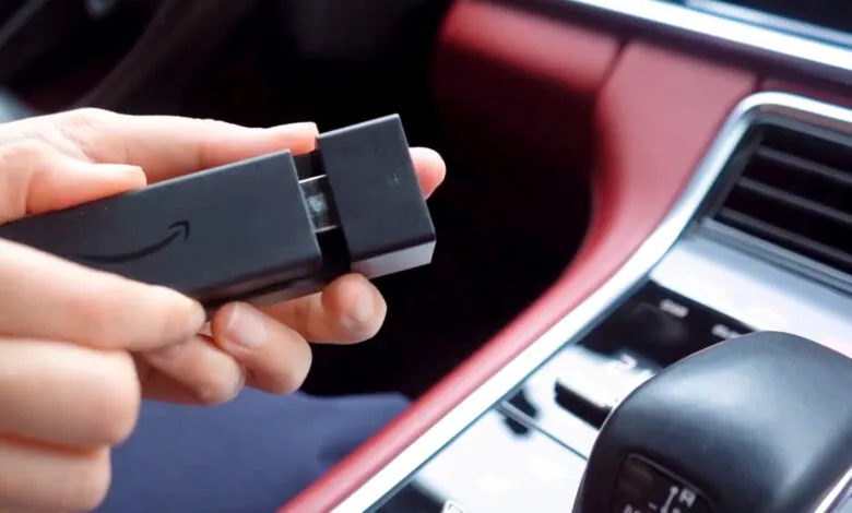 Hands hold Amazon Fire Stick near car console, red interior.