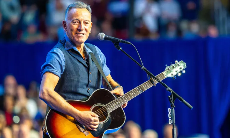 Bruce Springsteen smiles while playing guitar on stage.