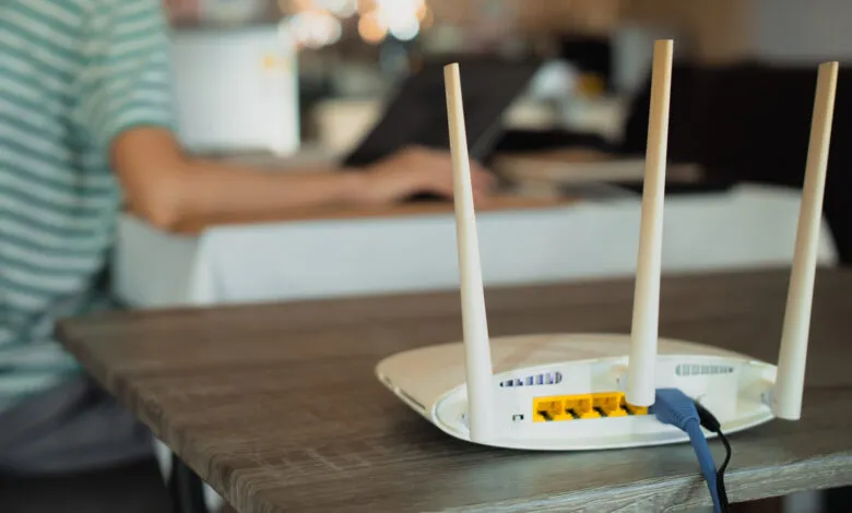 White wireless router with three antennas on a wooden table.