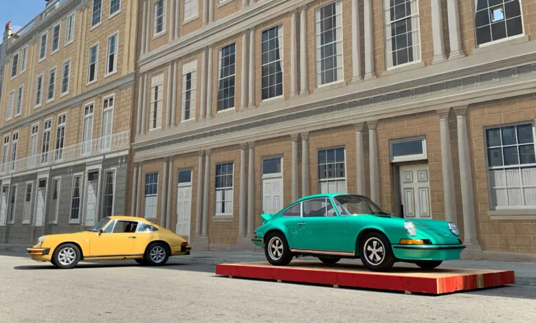 Yellow and teal Porsche 911s parked in front of a building facade.