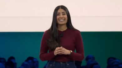 Woman with long dark hair smiles on stage at a presentation.