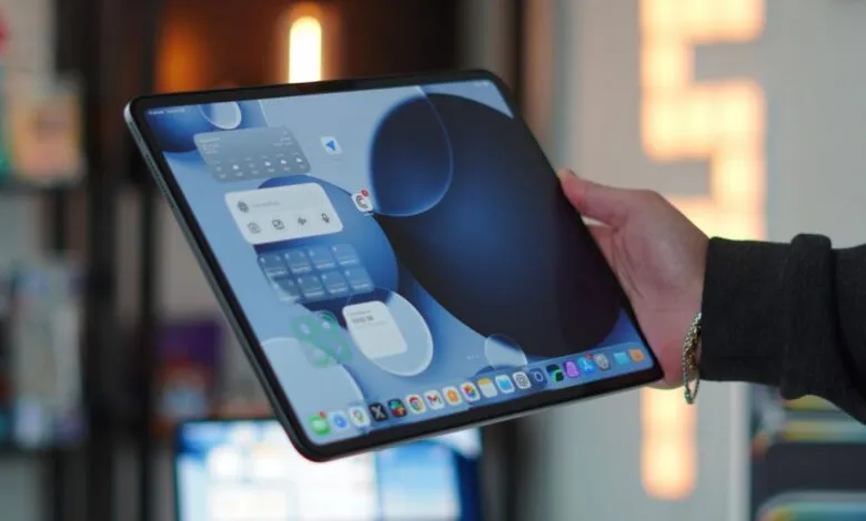 Person holds iPad Pro showing widgets and app icons on the screen.