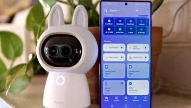 Aqara camera with bunny ears next to smartphone displaying smart home app.