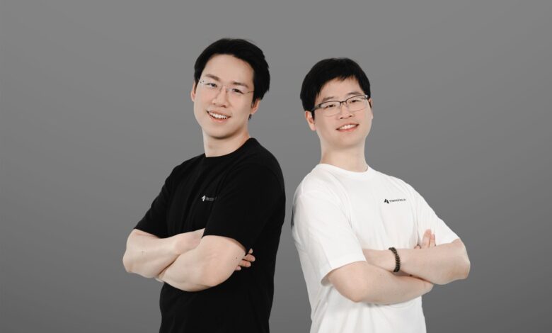 Two Asian men stand back-to-back, arms crossed, wearing Memories.ai shirts.