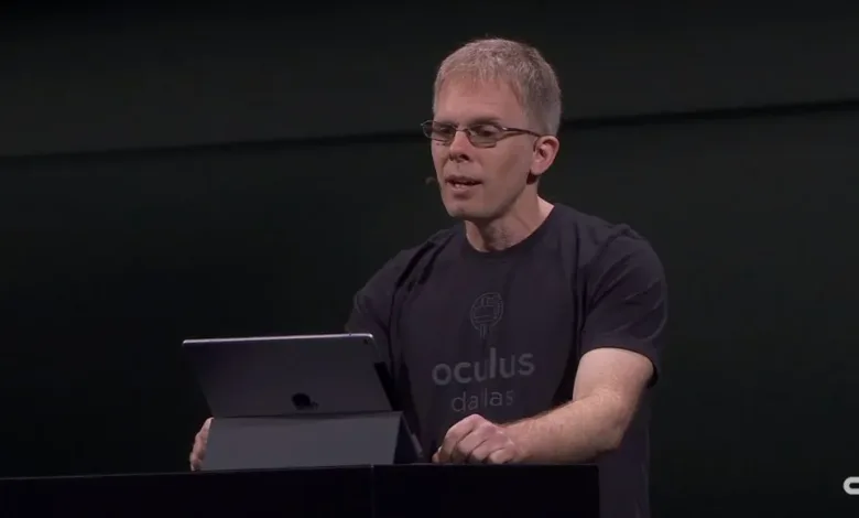 John Carmack speaking at a conference, holding a tablet.