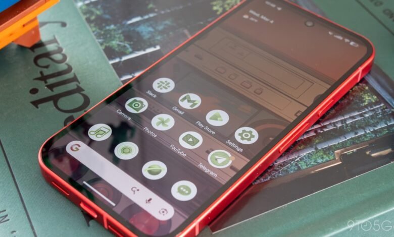 Red smartphone displaying app icons on its screen, resting on a book.