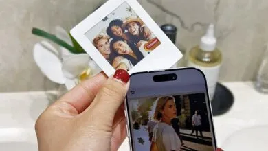 Hand holds phone displaying photo next to a printed instant photo of friends.