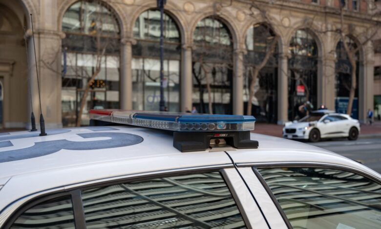 Police car with light bar and Waymo vehicle in urban setting.