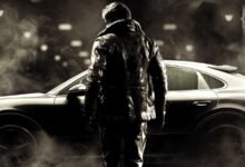 Man in leather jacket stands by a sleek Porsche car in the fog.