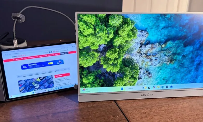 Handheld gaming PC next to a portable monitor displaying a coastal landscape.