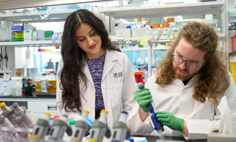 Two scientists in lab coats work with pipettes and microplates in a lab.