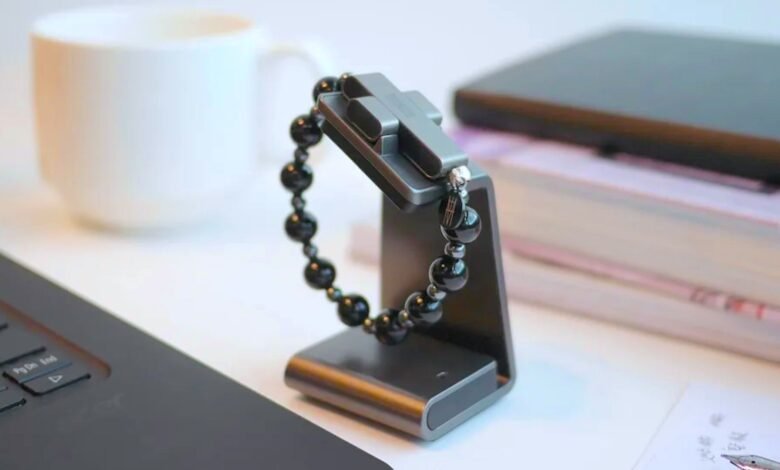 Black beaded bracelet displayed on a gray stand next to a laptop and mug.
