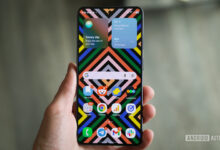 Hand holding smartphone with colorful geometric wallpaper and weather widgets.