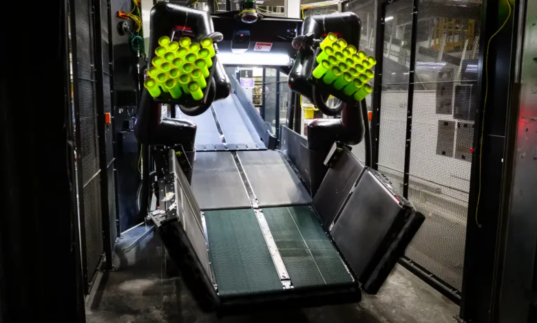 Robotic arms hold green tubes over a conveyor belt in a dark, industrial setting.