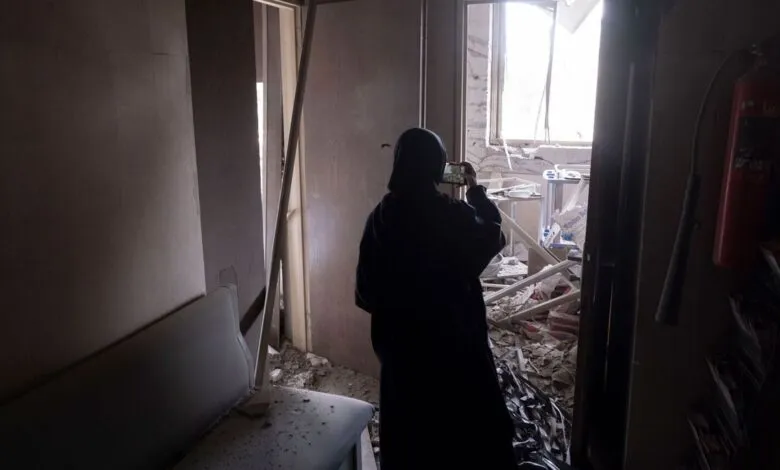 Person in hijab photographs room devastated by damage, debris visible.