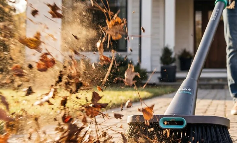 Person using Shark AUTOSENSE sweeper to clear leaves on a brick walkway.