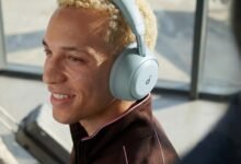 Person smiling, wearing light blue Soundcore Space 2 headphones in airport.