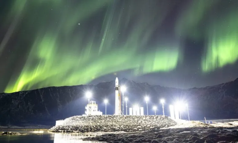 Rocket on launchpad under vibrant green aurora borealis.
