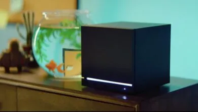 Black cube device sits on a wooden surface next to a fishbowl.