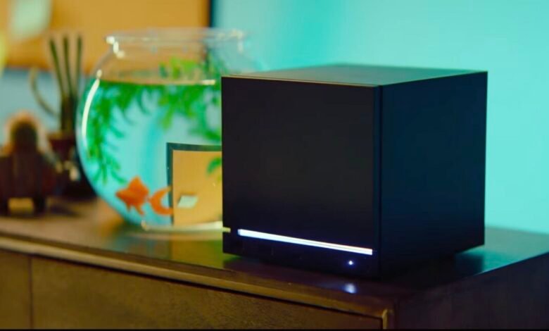 Black cube device sits on a wooden surface next to a fishbowl.