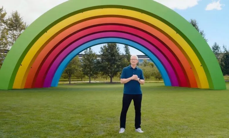 Tim Cook stands before a large rainbow structure on a green lawn.