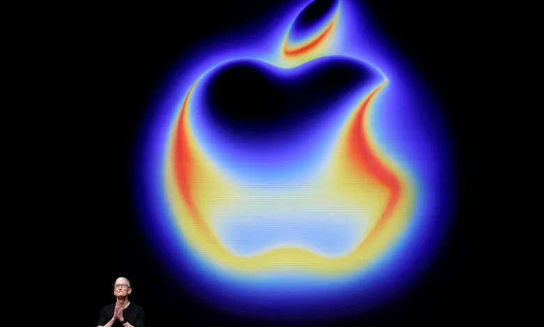 Tim Cook stands before a large, glowing Apple logo on a dark screen.