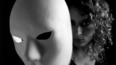 Black and white portrait of a woman partially obscured by a white mask.