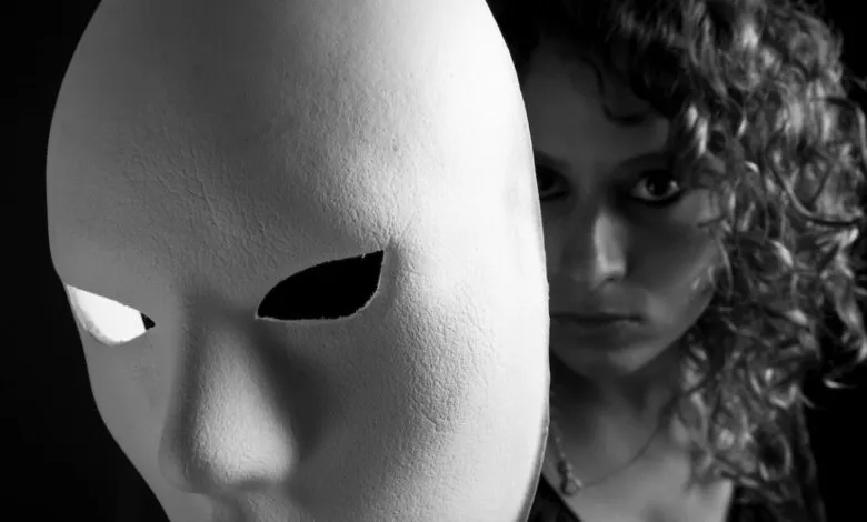 Black and white portrait of a woman partially obscured by a white mask.