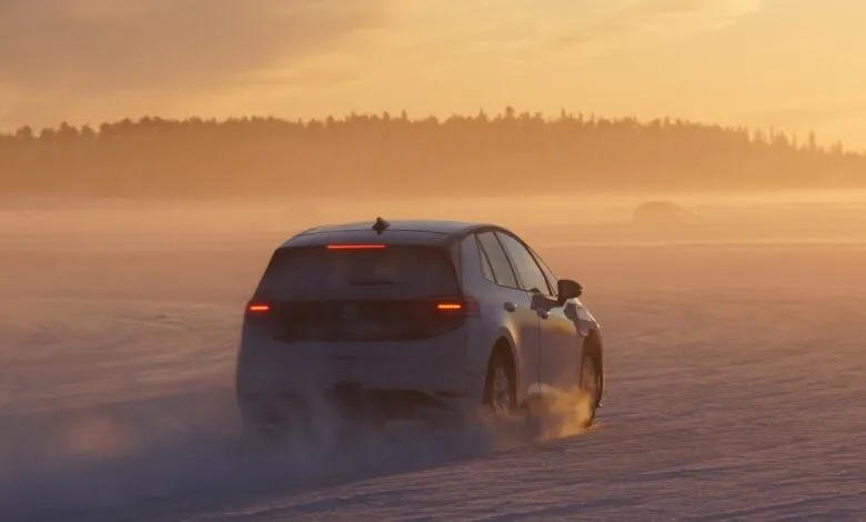 White electric car driving on snow-covered field at sunset.