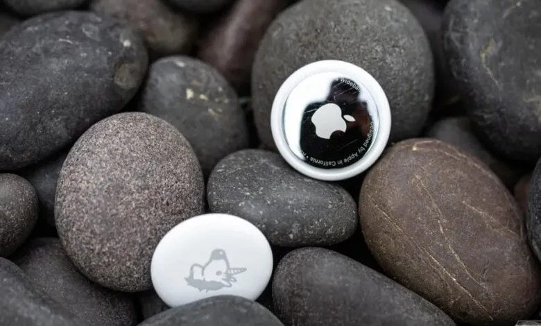 Apple AirTags nestled among smooth, dark river stones. One has a unicorn design.