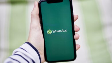 Hand holding smartphone displaying the WhatsApp logo on a green screen.