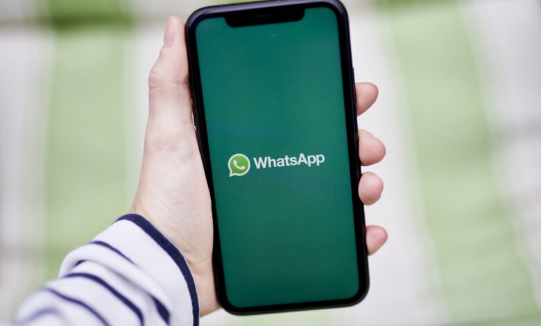 Hand holding smartphone displaying the WhatsApp logo on a green screen.