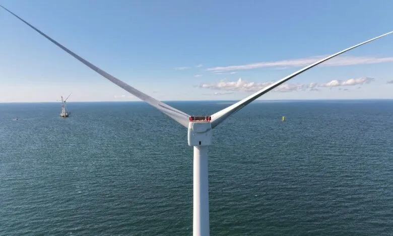 Close-up of a wind turbine in the ocean with two blades visible against a blue sky.