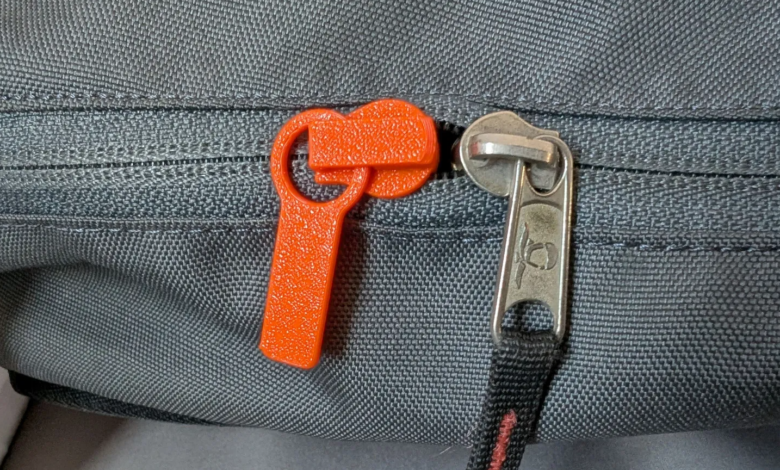 Close-up of gray fabric with orange and silver zipper pulls.