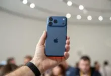 Hand holding a blue iPhone with three camera lenses.