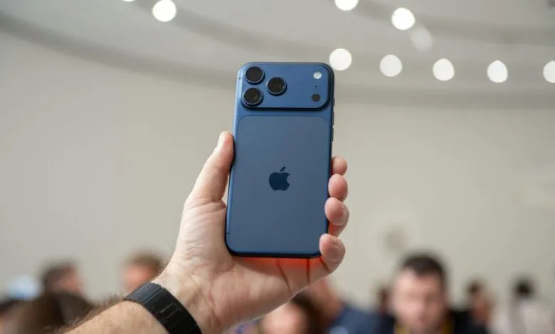 Hand holding a blue iPhone with three camera lenses.