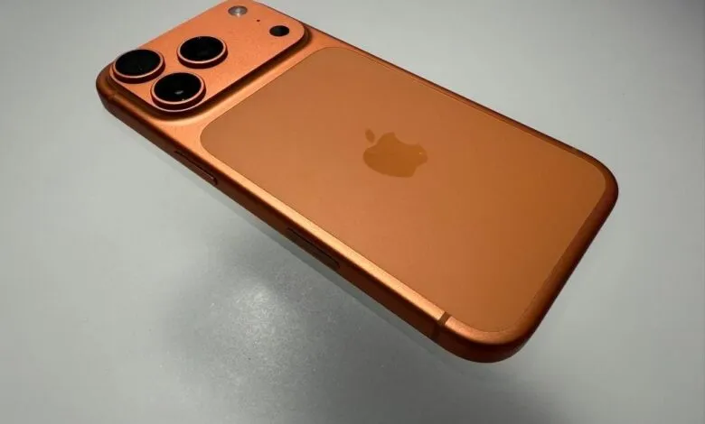 Close-up of an orange iPhone with three rear cameras on a gray surface.
