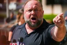 Alex Jones passionately speaks at a press conference, pointing forward.