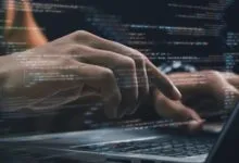 Hands typing on laptop with code overlay, suggesting software development or programming.